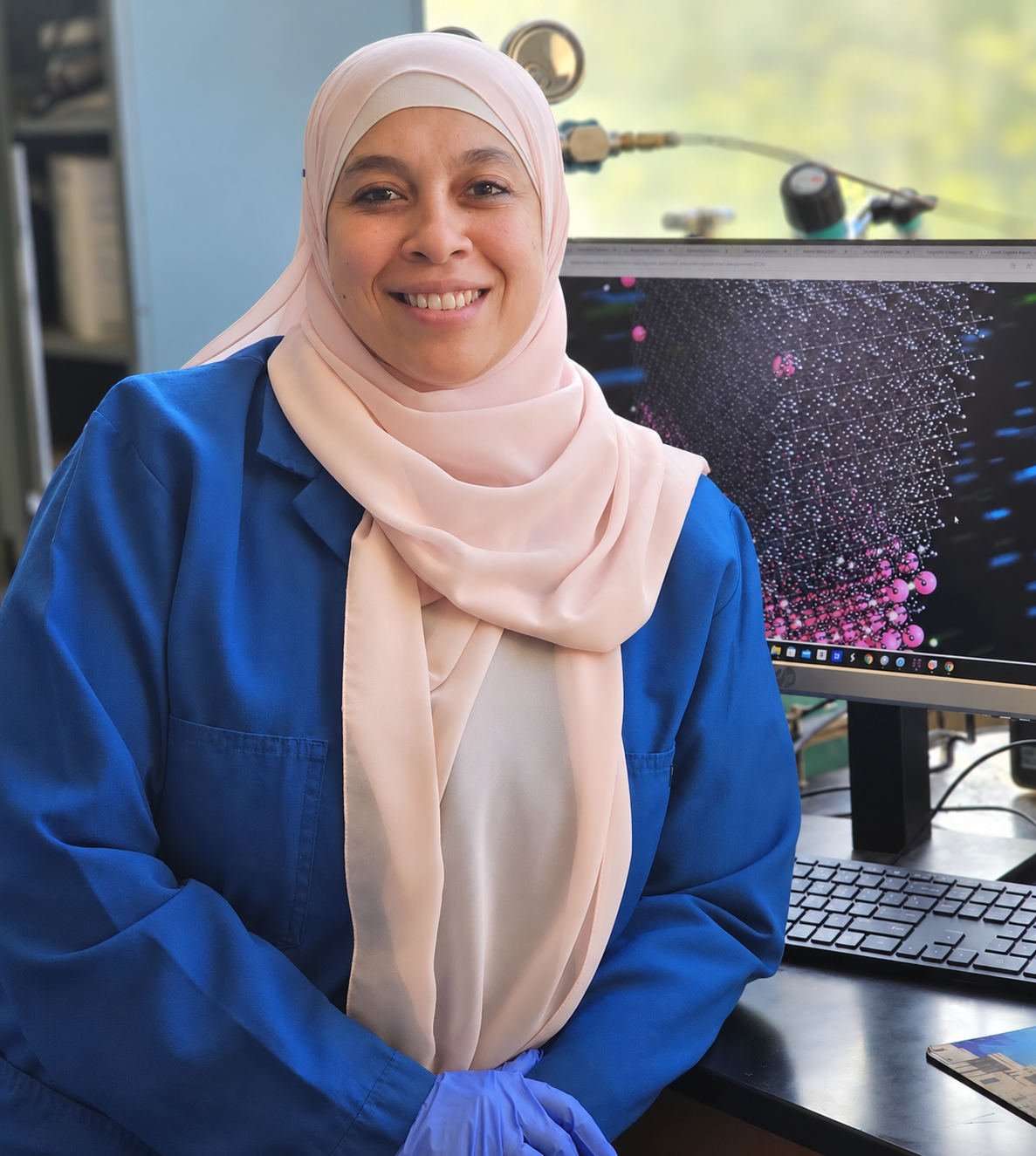 Dr. Mona H. Mohamed in the laboratory beside a molecular visualization
